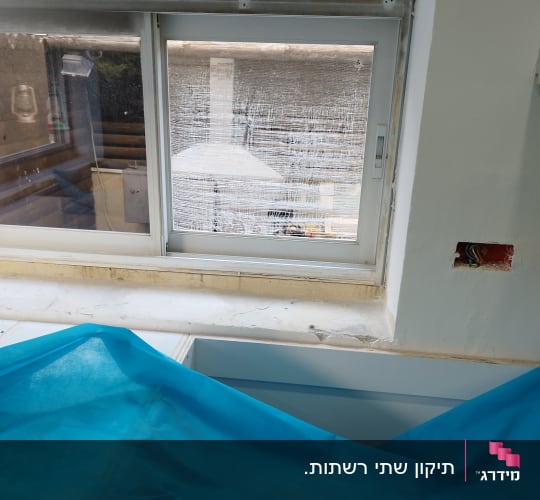 חלון עם תריסים סגורים למחצה ומסגרת לבנה